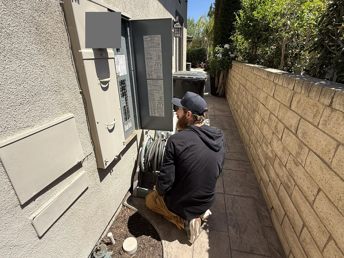 Technician kneeling at an open outdoor electrical panel in a side yard