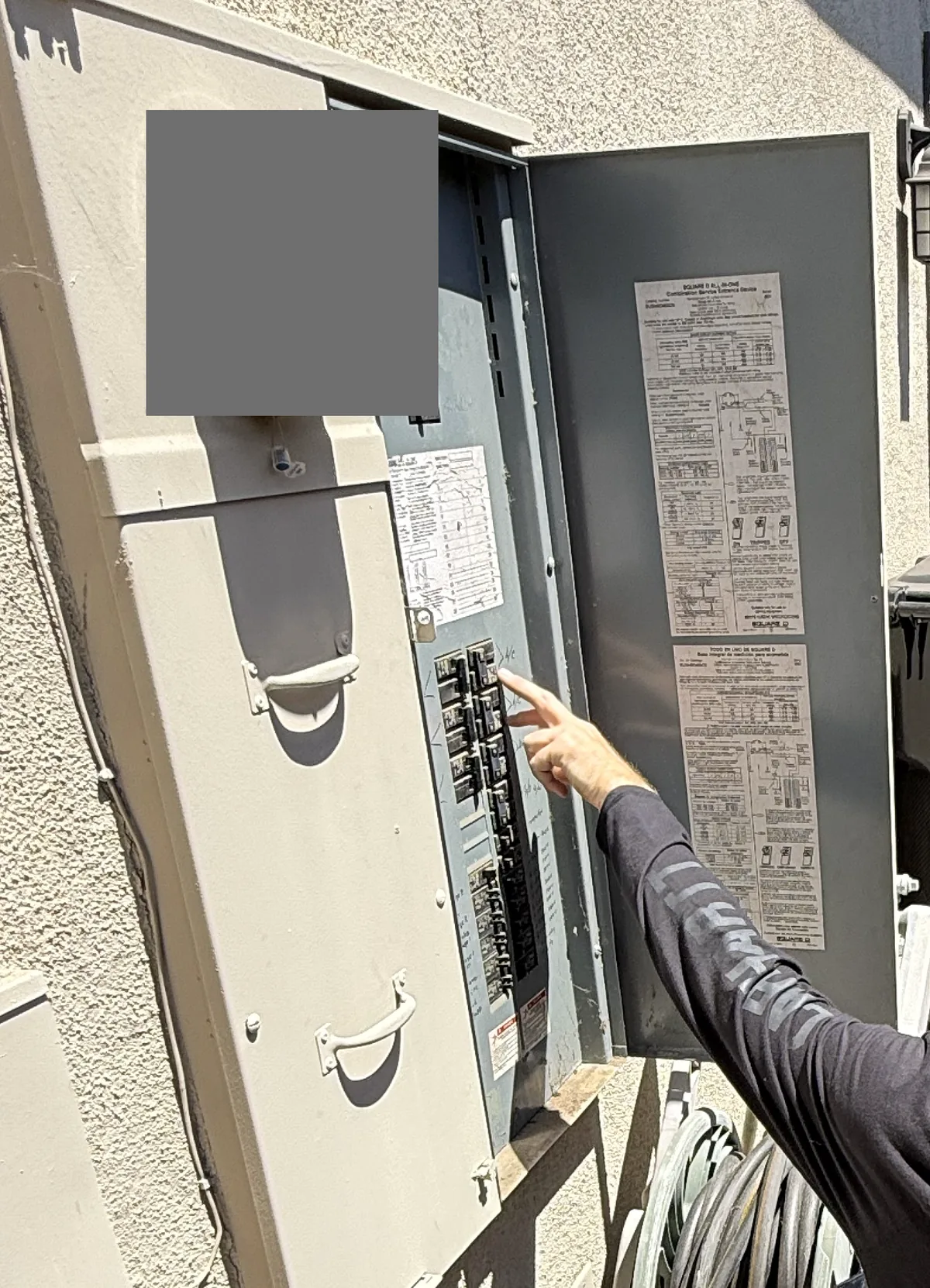 Hand pointing to a breaker in an open outdoor electrical panel